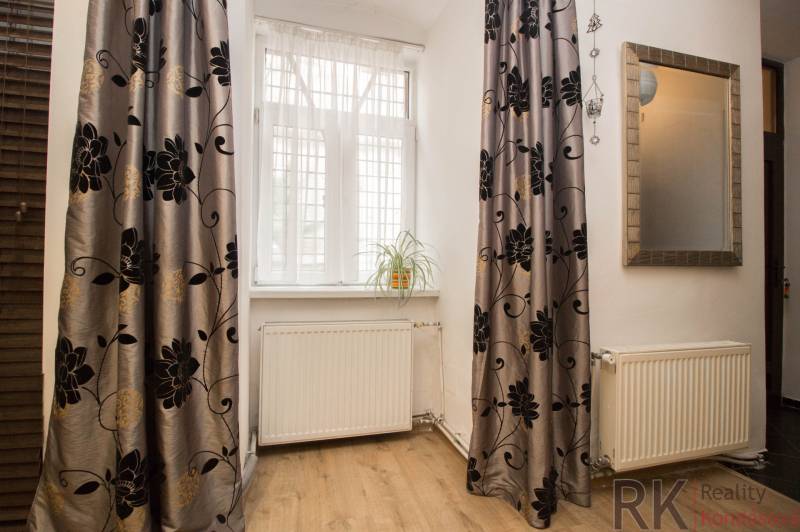 A room in a 2-room apartment with a floor featuring a wood decor, curtains, and a plant on the windowsill.
