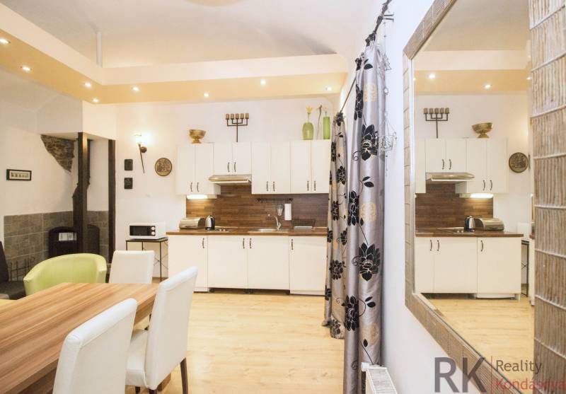 The kitchen of a 2-room apartment with a wooden decor floor, white cabinets, and a table.