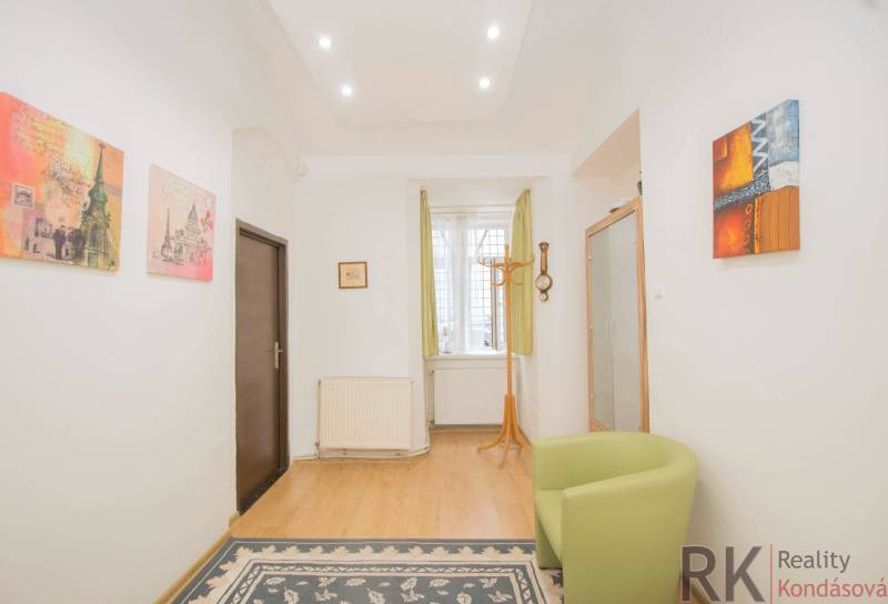 Interior of a 2-room apartment with a wooden decor floor, an armchair, and colorful paintings.