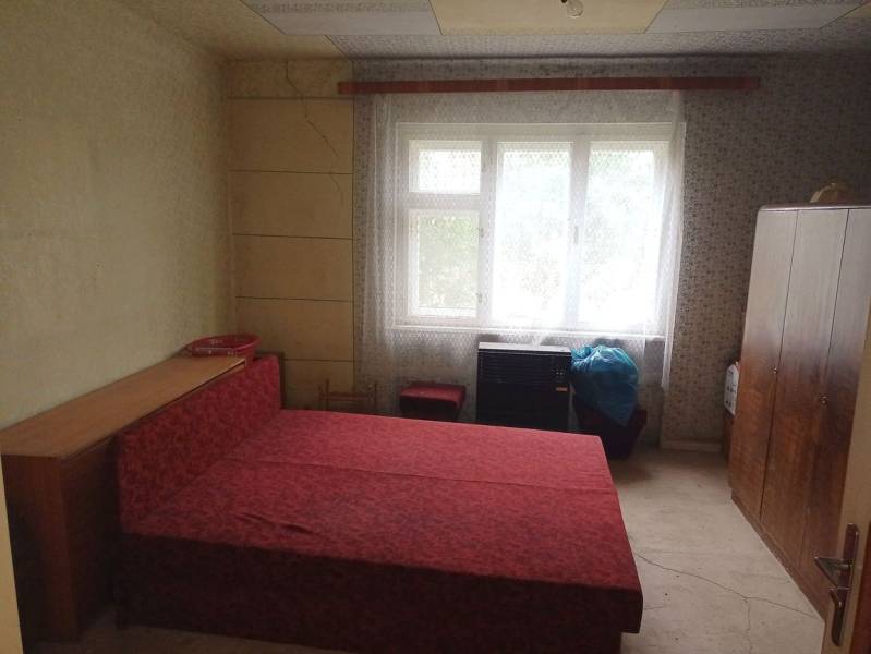 A bedroom in a family house with simple furniture and a red bed.