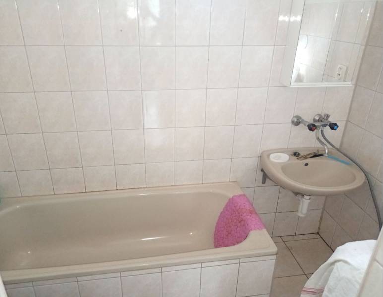 A bathroom with a bathtub and a sink in a family house, with light tiles and flooring.