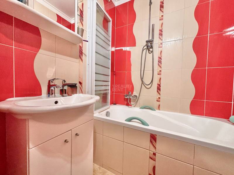 A bathroom with colorful tiles and a bathtub in a 2-room apartment.