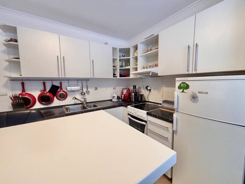 A kitchen in a 2-room apartment with light cabinets and red kitchen utensils.