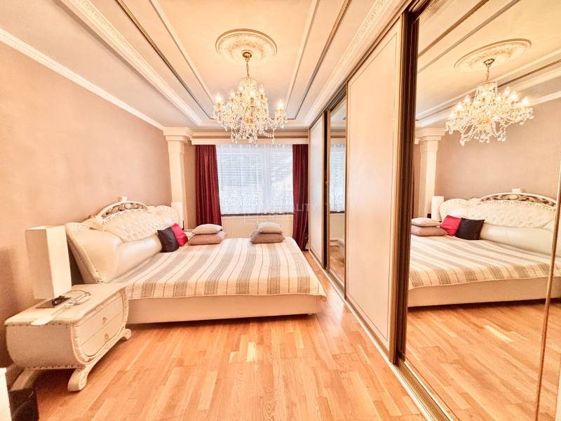 A bedroom with a chandelier, a large bed, and a floor with a wooden decor in a two-room apartment.