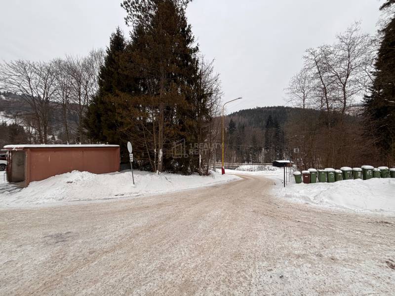 A snowy road in Oščadnica surrounded by trees and trash bins.
