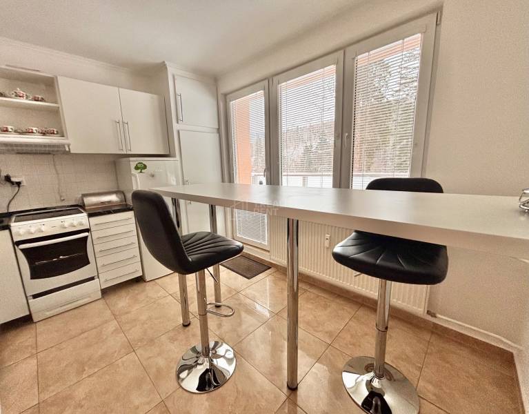 A kitchen in a 2-room apartment with a bar table, chairs, and white kitchen cabinets.