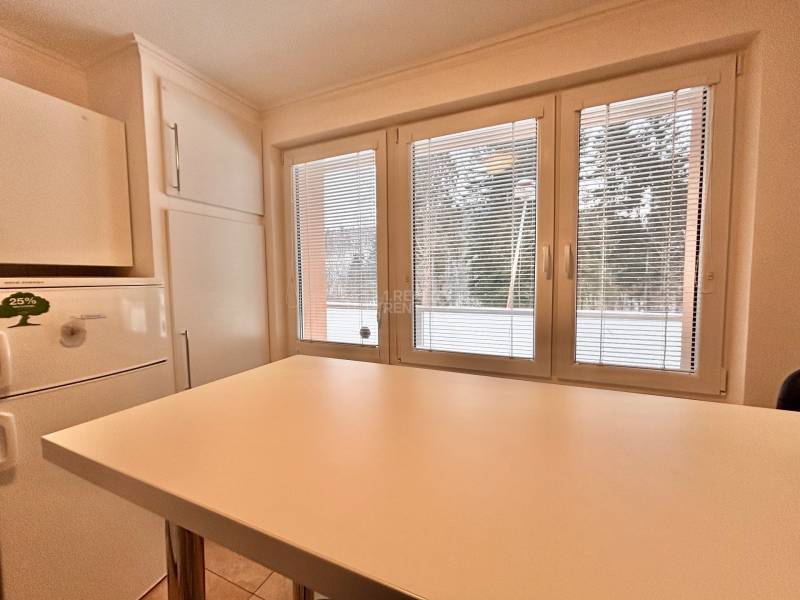 A kitchen in a 2-room apartment with a white table and a view through the window.