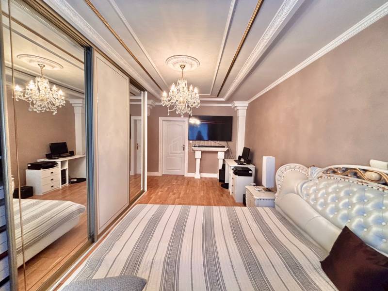 Bedroom in a two-room apartment with wood-patterned flooring and a large mirrored wardrobe.
