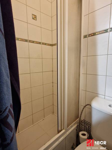 Bathroom in a studio apartment with a shower and a toilet, tiled with white tiles.