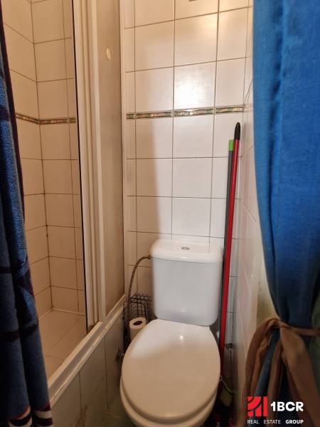 Bathroom in a studio apartment with a toilet and a shower corner, tiles with a decorative element.