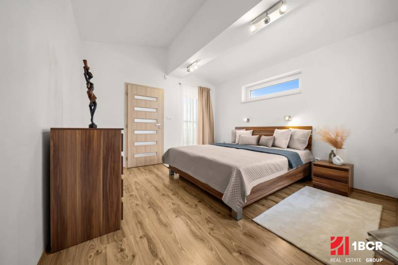 Bedroom with wood-patterned flooring, a bed, and a dresser in a family house.