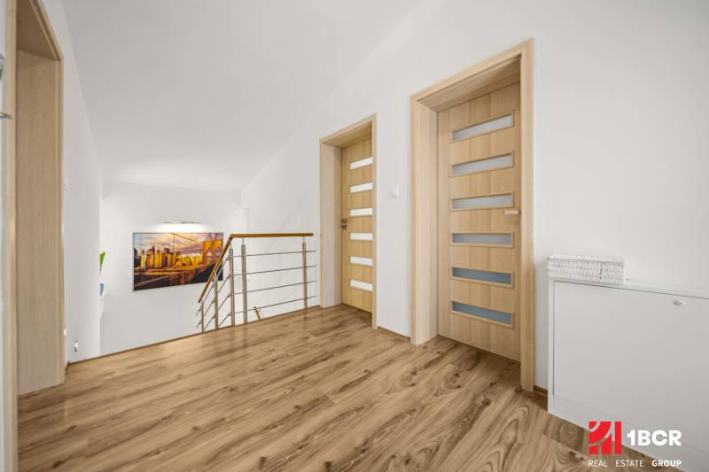 A hallway in a family house with a wooden decor floor, minimalist railing, and an art photograph.
