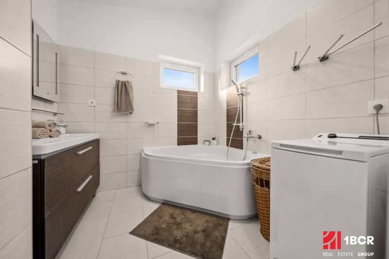 A bathroom in a family house with a bathtub, washing machine, brown and white tiles, and a cabinet.