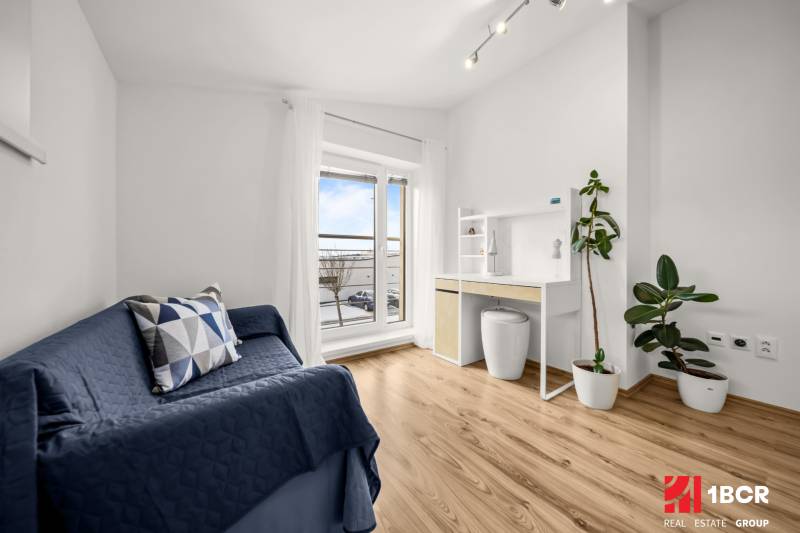 A room in a family house with a wooden decor floor, a blue sofa, and a desk.