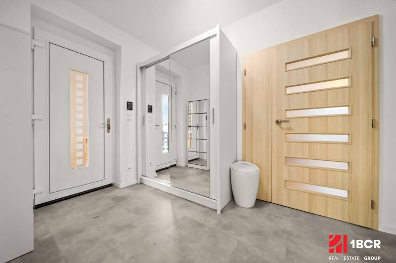 Entrance hall with wood-patterned flooring, mirrored wardrobe, and light-colored doors in a family house.