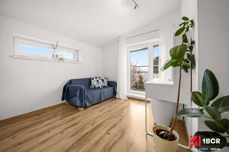 A room in a family house with a sofa, windows, and a wooden decor floor.