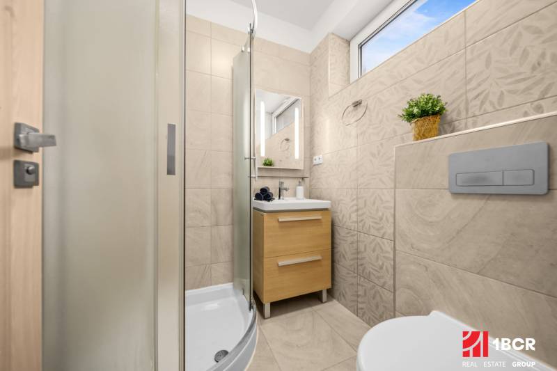A bathroom in a family house with a shower, a sink, and light-colored tiles.