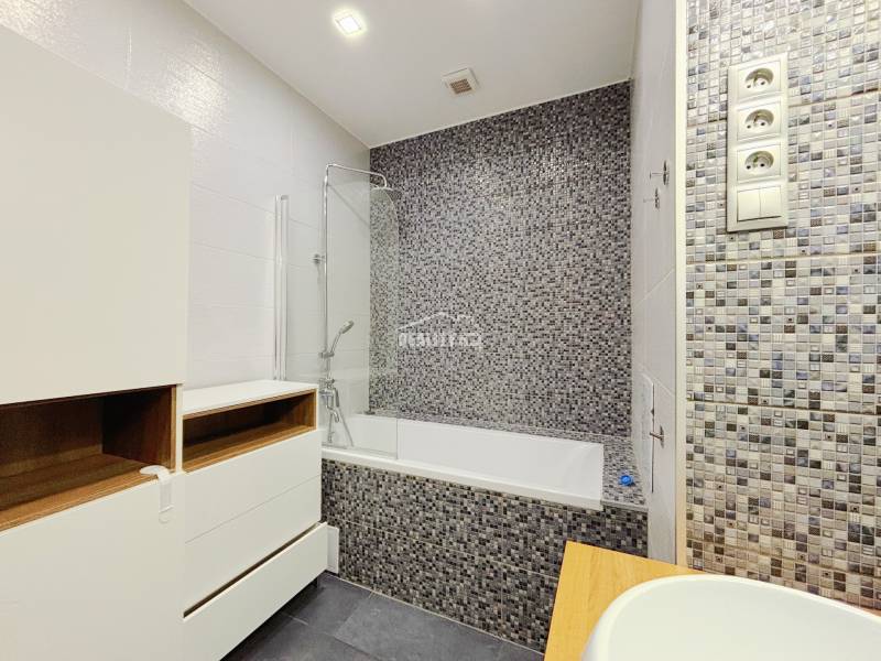 A bathroom in a 2-room apartment with a bathtub, mosaic tiles, and storage spaces.