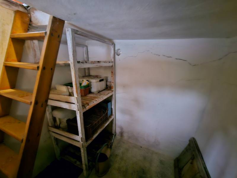 A storage space in a cabin with shelves and a ladder, the floor has cracks.