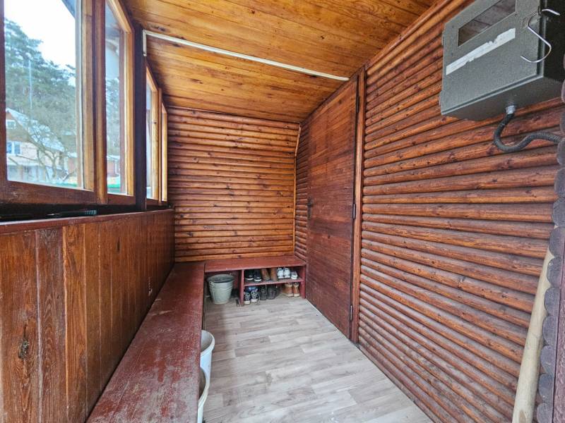 Wooden porch of the cottage with a wood-patterned floor and a storage bench.