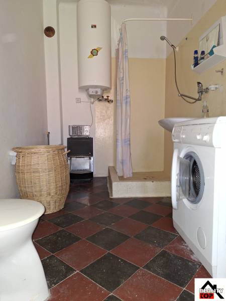 A bathroom in a family house with a washing machine, shower, boiler, and tiles.