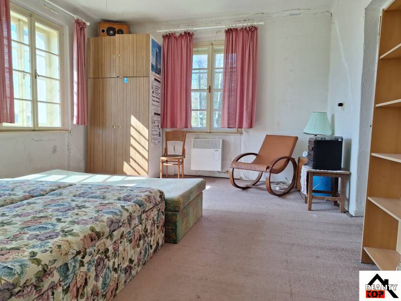 A room with a floral sofa, an armchair, a wardrobe, and pink curtains in a family house.