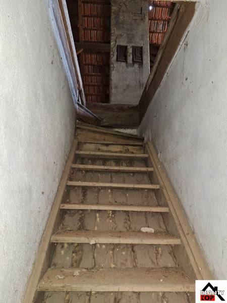 An old wooden staircase leads to the attic of a family house with a trapezoidal roof.