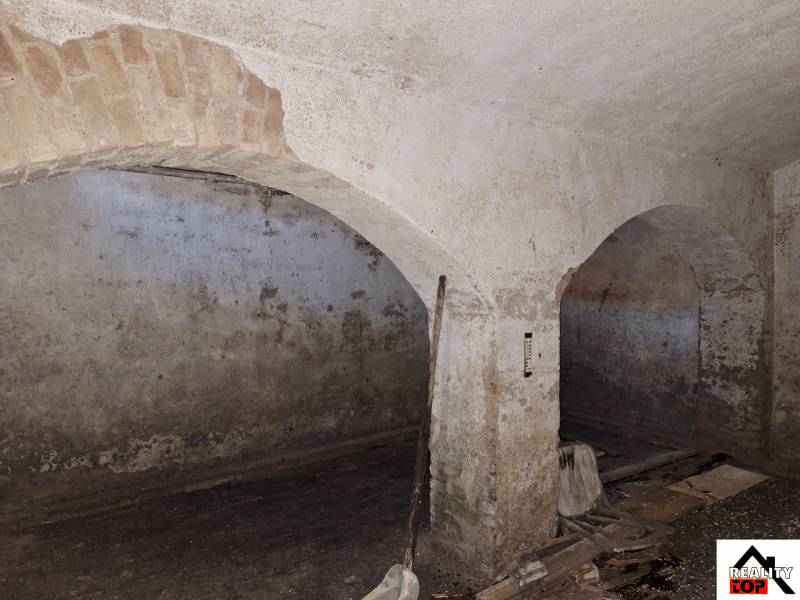 A stone cellar space in a family house with brick vaults and peeling plaster.