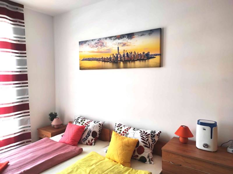 A bedroom in a holiday apartment with colorful pillows and a panorama painting.