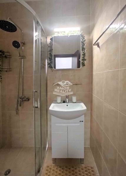 Bathroom in a holiday apartment with a shower and a sink, tiled with light tiles.