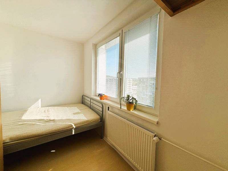 Bright bedroom with a bed, window, blinds, and wood-patterned flooring in a two-room apartment.