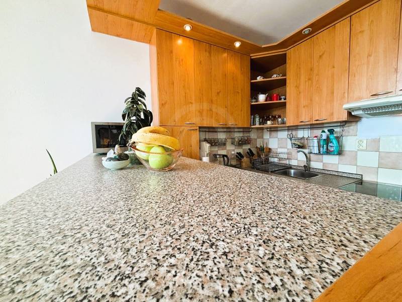 A kitchen in a 2-room apartment with a wooden decor and a fruit bowl on a stone countertop.