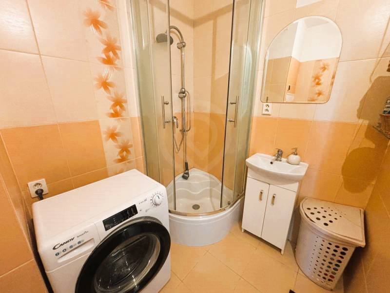 Bathroom with a washing machine, shower, sink, and orange tiles in a 2-room apartment.
