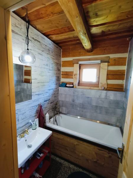 A bathroom in a cabin with a bathtub, a sink, wooden walls, and a simple light.