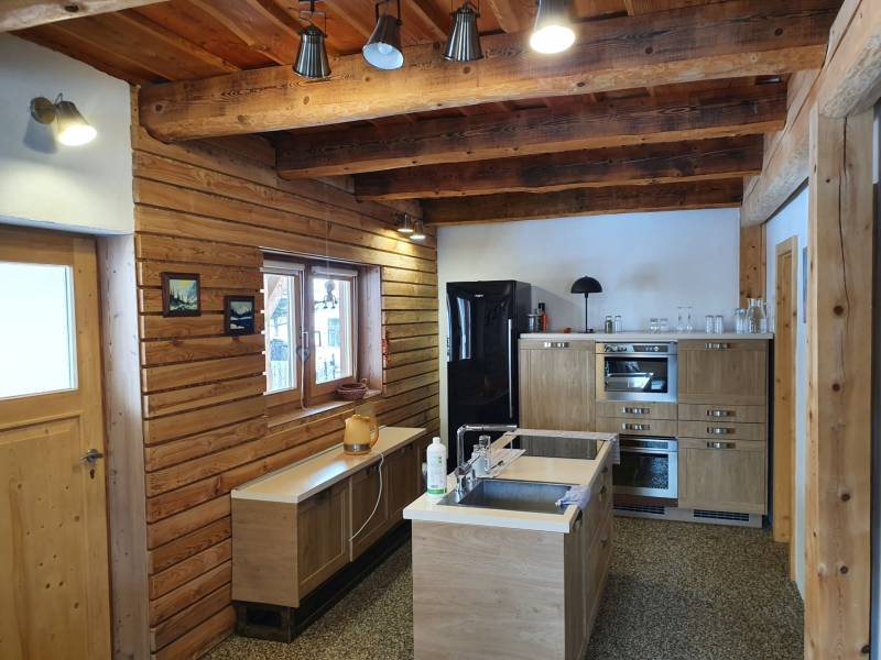 Rustic kitchen in a cottage with wooden decorations, light furniture, and ceiling beams.