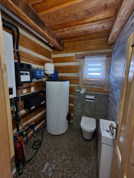 A bathroom in a cabin with a toilet, sink, and technical equipment. The interior is dominated by wood.