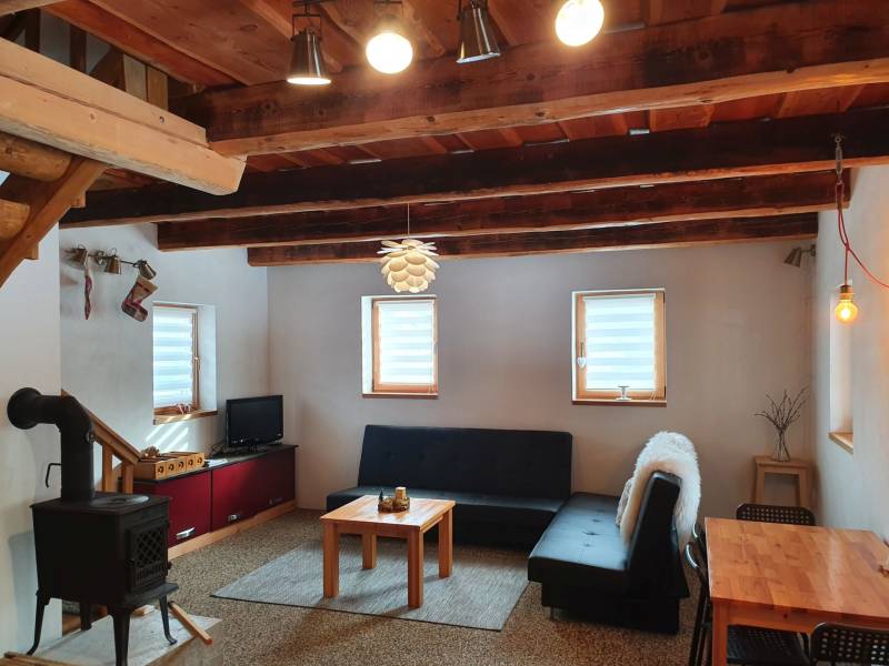 The interior of a cottage with a tiled stove, a sofa, and a wooden ceiling made of solid beams.