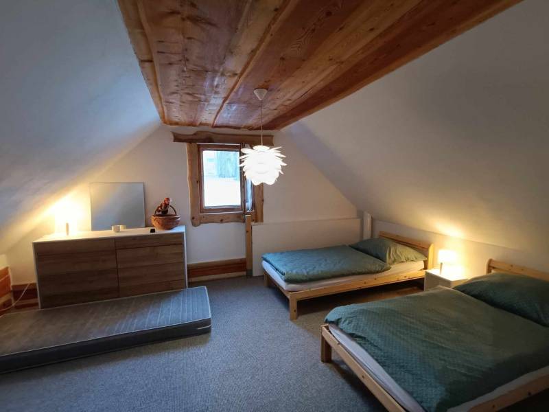 The attic of the cottage with two beds and a chest of drawers with a wooden decor.