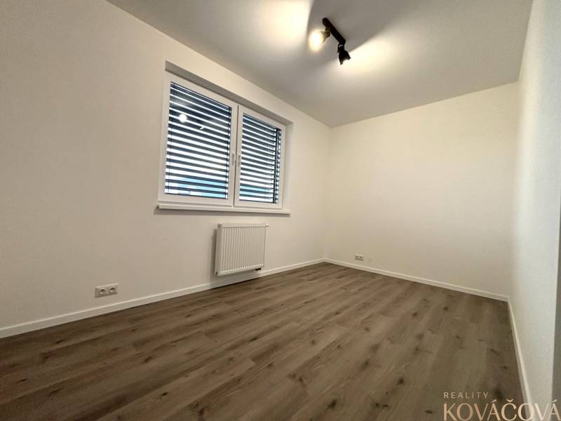 A room with a wooden decor floor in a 3-room apartment, white walls, and a radiator.