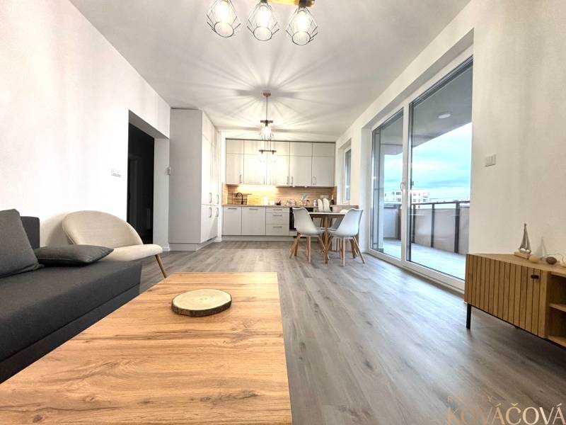 Living room with wood-patterned flooring and a dining table in a three-room apartment.