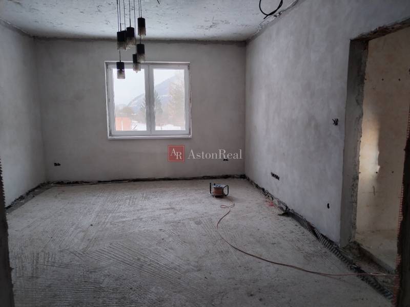 Room of an unfinished family house, bare walls, large window, concrete floor, hanging lights.