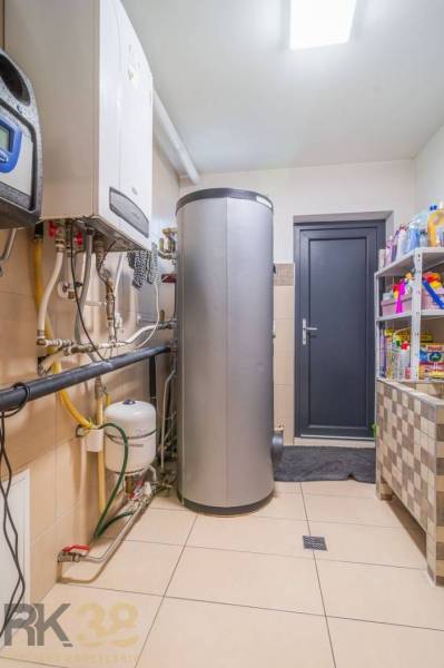 Technical room in a family house with a boiler, tank, and shelves with cleaning products.