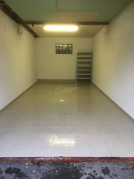 A view into an empty garage with gray tiles on the floor and a shelf in the back.