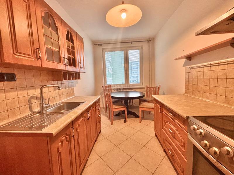 A kitchen in a 3-room apartment with brown cabinets, a dining table, and light tiles.