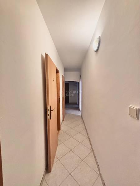 A hallway in a 3-room apartment with tiles, light, and wooden doors to the rooms.