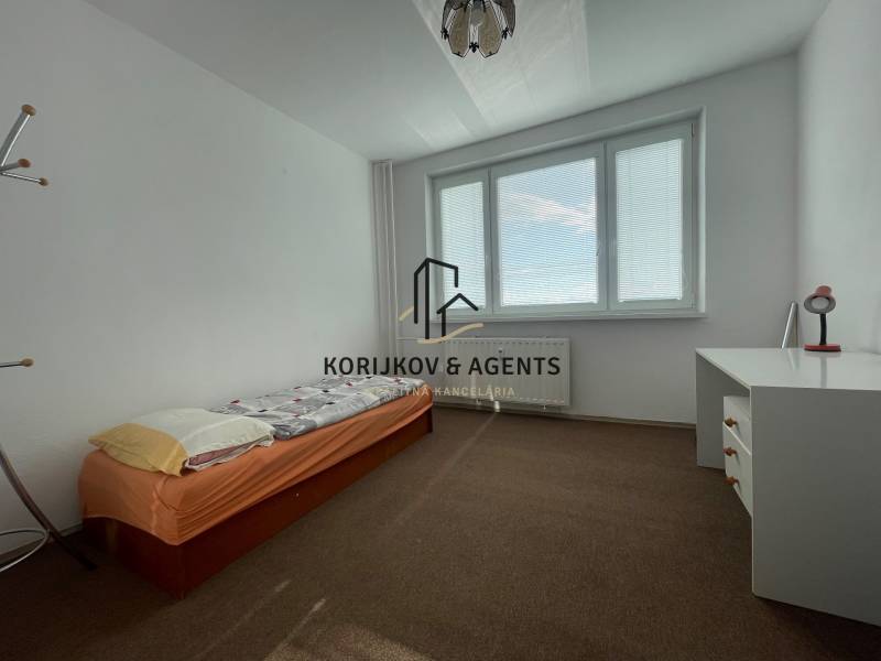 Simple bedroom with a bed, desk, and carpeted floor in a 3-room apartment.