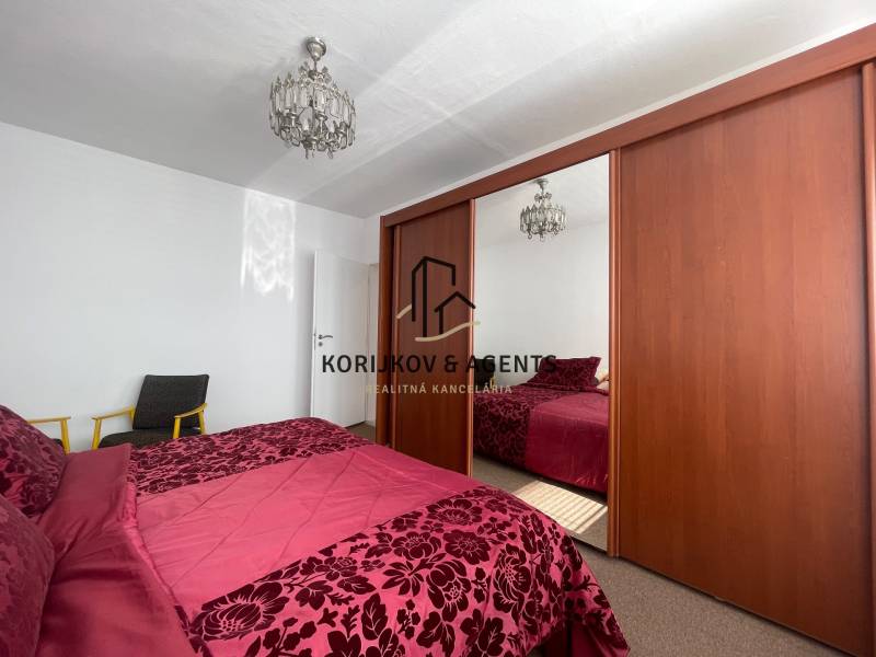 A bedroom with a large wardrobe, chandelier, and bed in a three-room apartment.