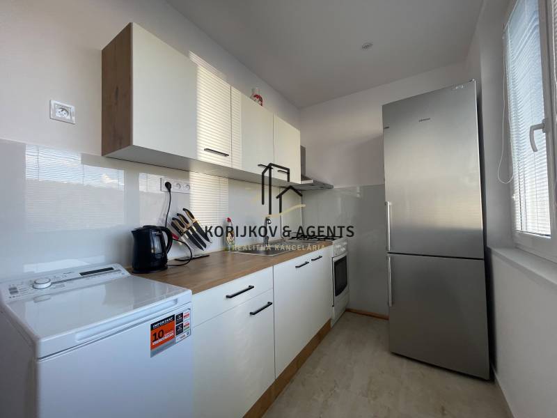 A kitchen in a 3-room apartment with white cabinets and a stainless steel refrigerator.