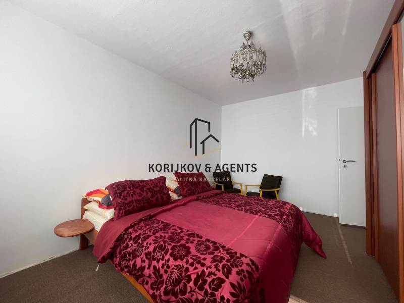 Bedroom with a bed with patterned bedding, ceiling light, and wardrobe in a 3-room apartment.