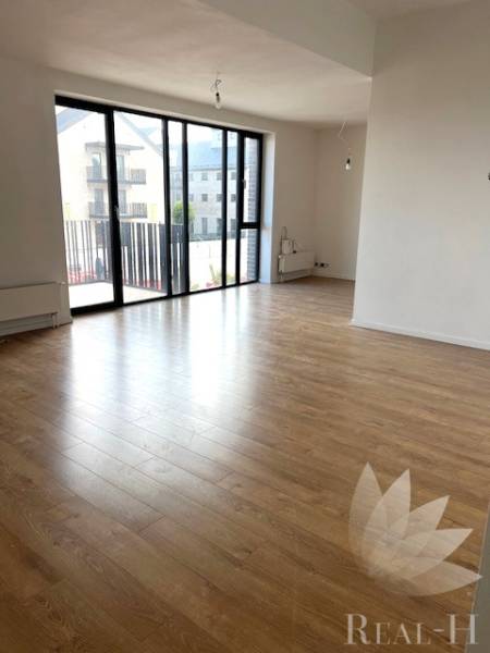 Spacious living room in a 2-room apartment with wood-patterned flooring and large windows.